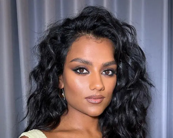 Capelli neri e ondulati, lucidi grazie al hair oiling, incorniciano il viso di una donna con trucco intenso.