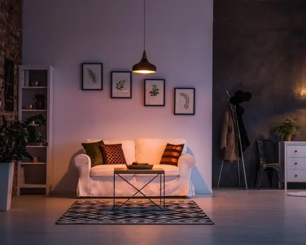 Un divano bianco accogliente, con cuscini colorati, in un soggiorno con mattoni a vista e quadri botanici. Atmosfera di puro stile cozy.