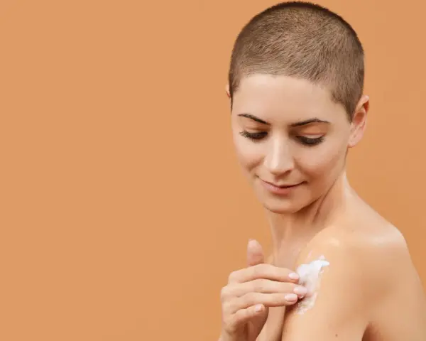 Donna con capelli corti applica crema idratante al burro di karitè viso sulla spalla, per una pelle morbida e nutrita.