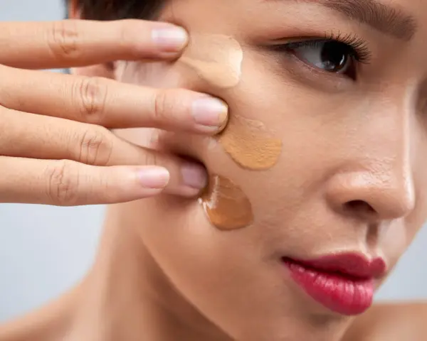 Dita che sfumano campioni di fondotinta sulla guancia per capire come scegliere il colore del fondotinta perfetto.