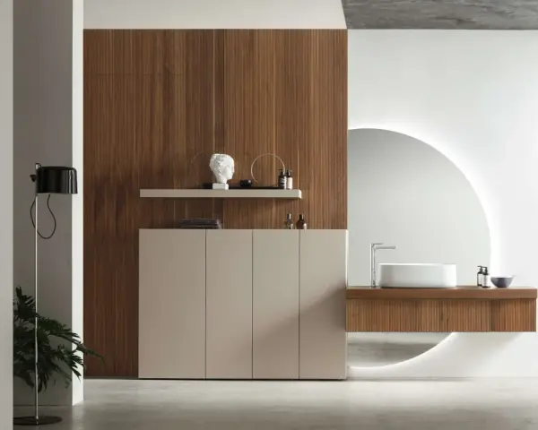 Bagno elegante e raffinato con mobile in legno, lavabo sospeso, specchio circolare retroilluminato e un tocco di verde da una pianta.
