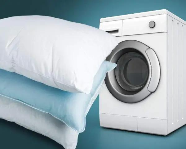 Impara come lavare i cuscini in lavatrice per un sonno fresco e igienico. Cuscini bianchi e azzurri accanto a una lavatrice bianca.