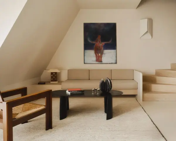 Arredamento minimal soggiorno: poltrona in legno e paglia, divano beige, tavolino nero con libri e scultura, quadro astratto con toro.