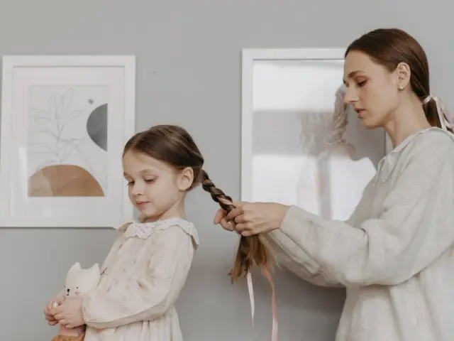 Mamma intreccia i capelli della bambina, creando bellissime acconciature. La piccola tiene un pupazzo a forma di gatto.