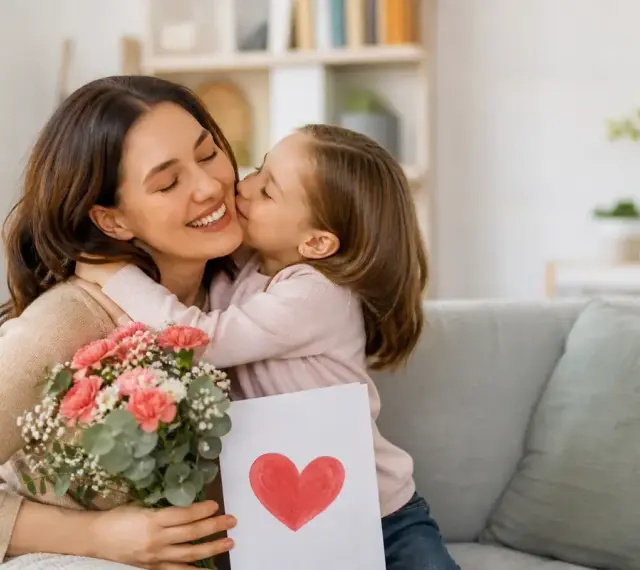 Bambina bacia la mamma, regalandole fiori e un disegno a forma di cuore. Un dolce momento per la festa della mamma.