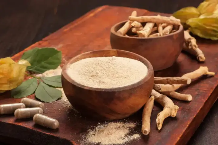 Radici, polvere e capsule di ashwagandha su tagliere di legno. Scopri come assumere ashwagandha per il benessere.