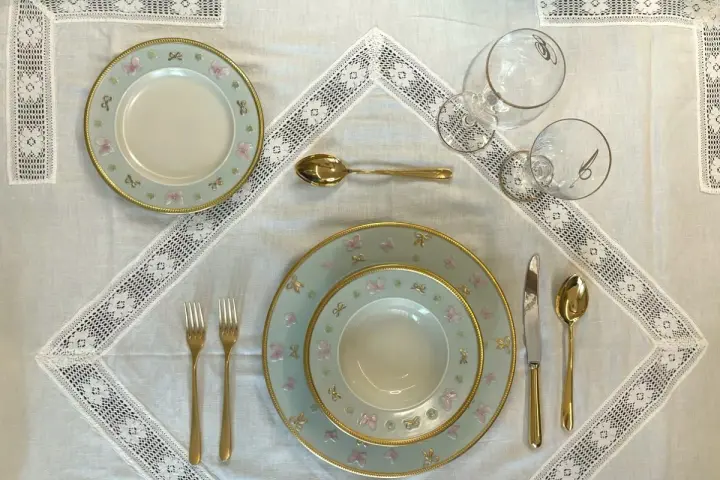Tavola apparecchiata con piatti azzurri decorati con farfalle rosa e fiocchi, posate dorate e bicchieri eleganti. Idee tavola apparecchiata per un'occasione speciale.