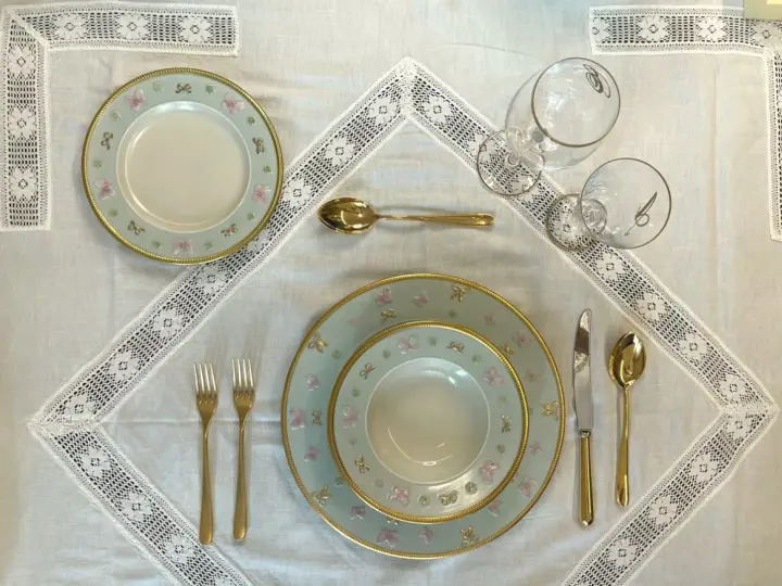 Tavola apparecchiata con piatti azzurri decorati con farfalle rosa e fiocchi, posate dorate e bicchieri eleganti. Idee tavola apparecchiata per un'occasione speciale.