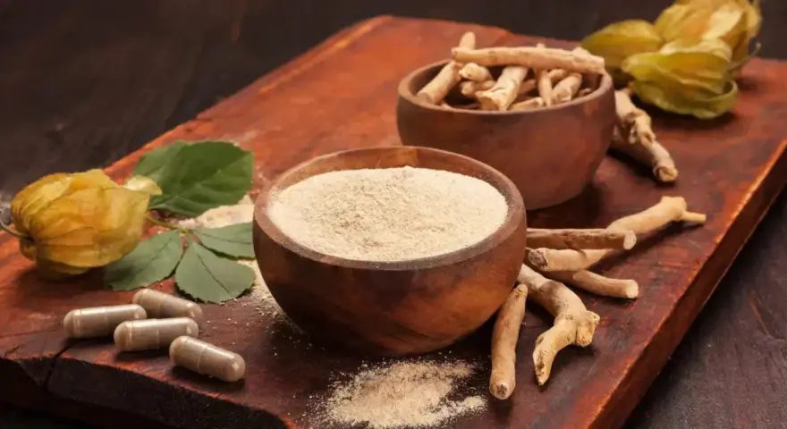 Radici, polvere e capsule di ashwagandha su tagliere di legno. Scopri come assumere ashwagandha per il benessere.