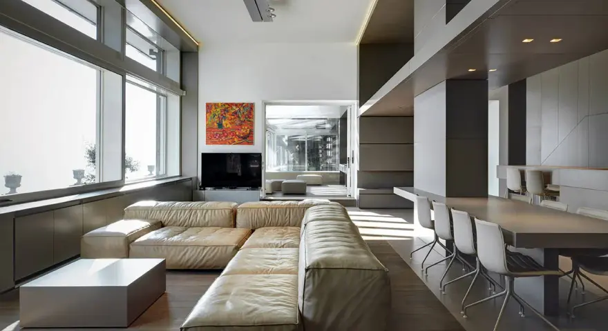 Un ampio soggiorno moderno, perfetto per arredare soggiorno grande, con divano componibile in pelle chiara, tavolino squadrato e zona pranzo con tavolo lungo e sedie di design.