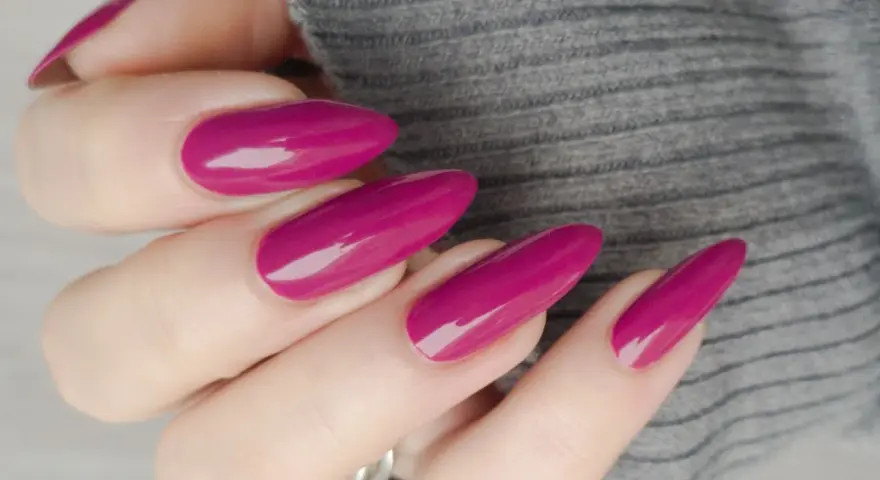 Mano con unghie lunghe e affusolate, smalto color ciliegia brillante, su sfondo grigio melange.