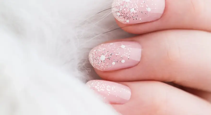 Unghie natalizie rosa pastello con brillantini scintillanti e decorazioni a stella, su sfondo bianco soffice.