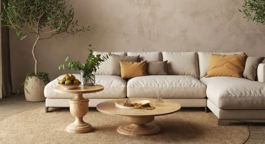 Soggiorno beige e bianco con divano modulare, tavolini in legno, piante e tappeto in juta.