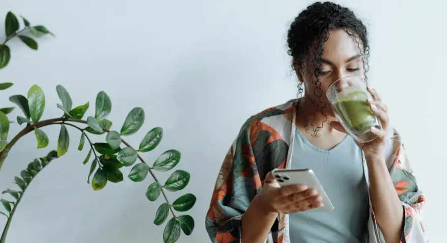 Donna con capelli ricci beve un tè verde mentre guarda il telefono, ignara che il tè fa ingrassare.