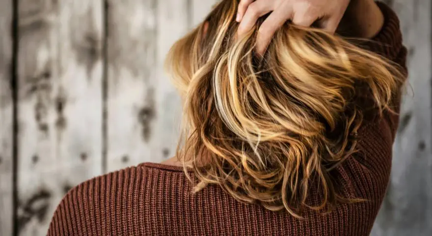 Mano tra i capelli biondi e mossi, che ricadono morbidi sulle spalle.