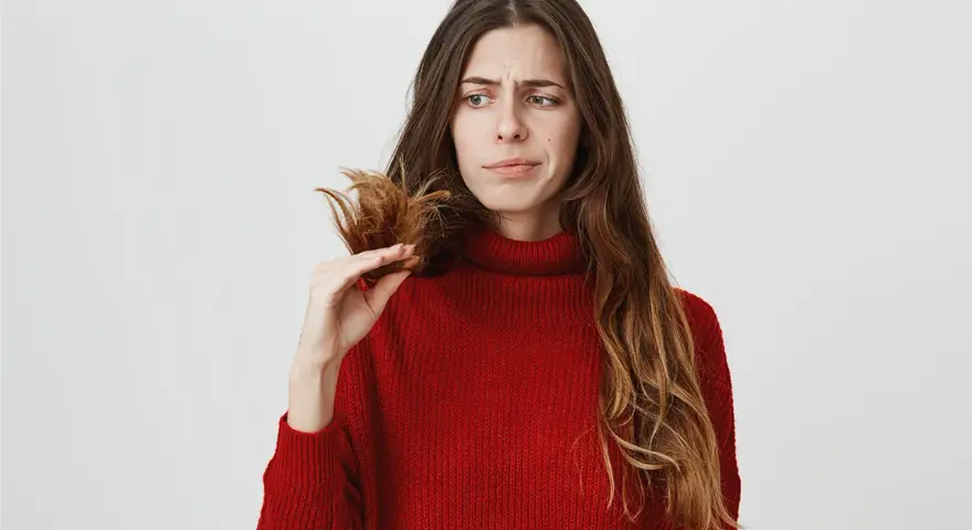Donna preoccupata guarda le doppie punte, pensando a come nutrire i capelli per renderli sani e forti.