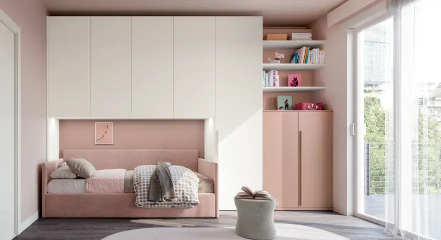 Camera ragazza aesthetic con letto rosa, armadio bianco e rosa, libreria con libri e decorazioni, pouf e grande finestra.