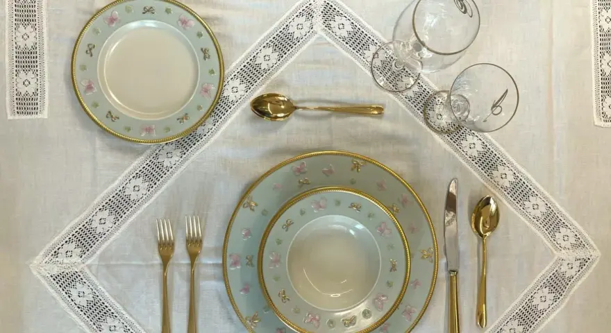 Tavola apparecchiata con piatti azzurri decorati con farfalle rosa e fiocchi, posate dorate e bicchieri eleganti. Idee tavola apparecchiata per un'occasione speciale.