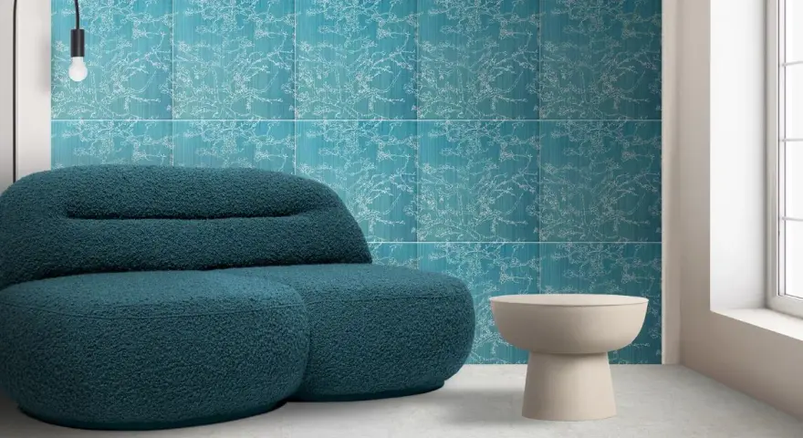 Divano blu petrolio davanti a una parete con motivo floreale su sfondo colore verde acqua. Tavolino beige e lampada nera.