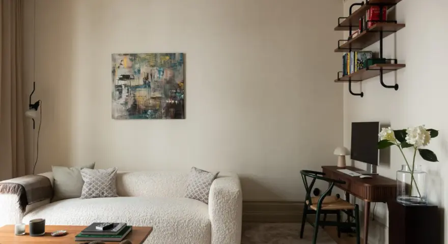 Soggiorno accogliente con divano bouclé bianco, quadro astratto e scrivania. Le **pareti colore crema** creano un'atmosfera calda e rilassante.