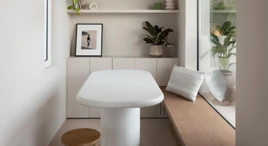 Un angolo accogliente con tavolo bianco, sgabello in legno e piante. Un'ispirazione su come combattere la solitudine in casa, creando spazi piacevoli.