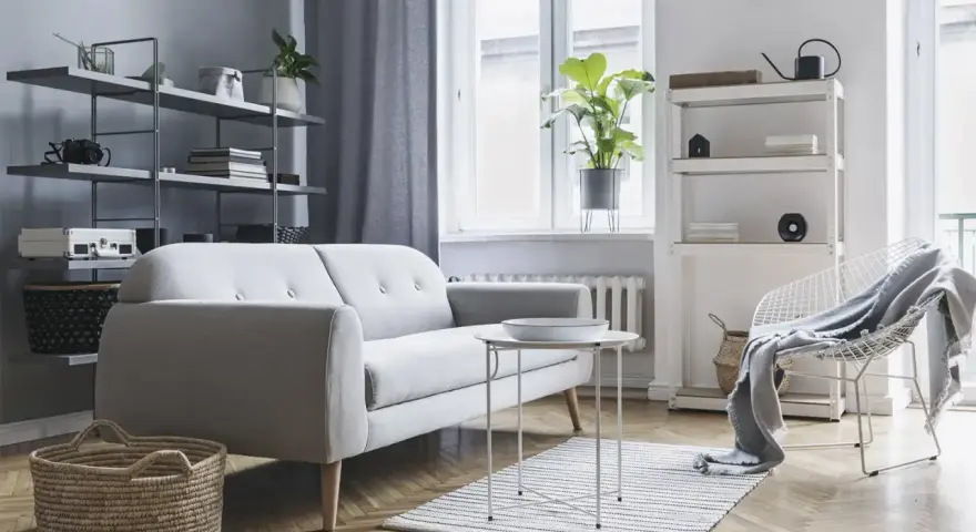 Soggiorno moderno con divano grigio, tavolino bianco, cestini in paglia e scaffali pieni di oggetti. Ottime idee arredamento casa per uno stile minimalista.