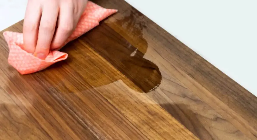 Mano che pulisce un tagliere di legno con un panno umido. Scopri come pulire il tagliere di legno per mantenerlo igienico e bello.