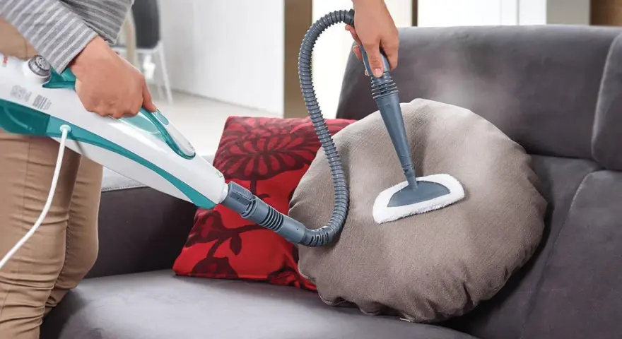Persona usa un pulitore a vapore per pulire un cuscino del divano in tessuto. Scopri come pulire divano in tessuto con questo metodo efficace.