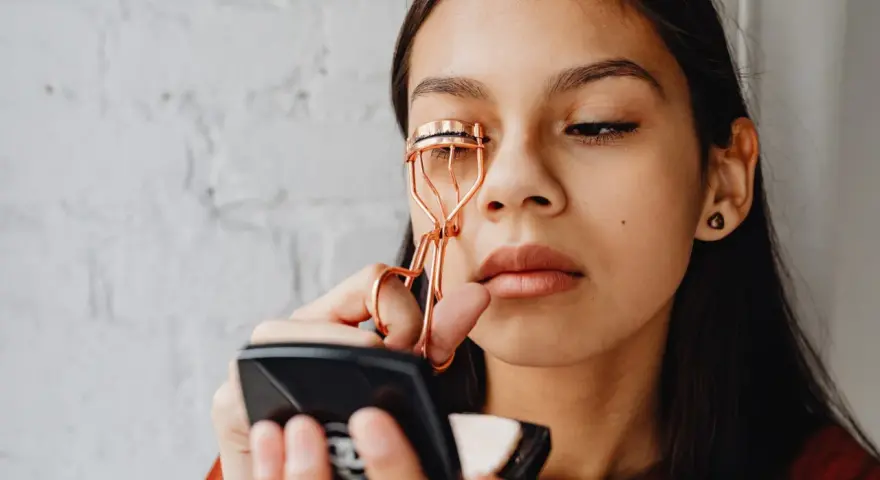 Ragazza usa un piegaciglia dorato, sperando che non rovina le ciglia.