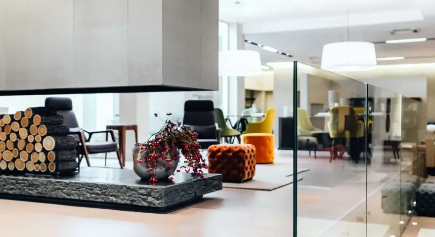 Interni open space di case moderne: camino con legna, vasi con bacche rosse, sedie colorate e pouf arancioni in un ambiente luminoso.