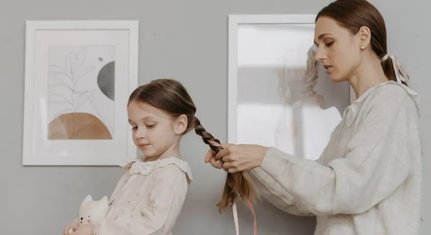 Mamma intreccia i capelli della bambina, creando bellissime acconciature. La piccola tiene un pupazzo a forma di gatto.