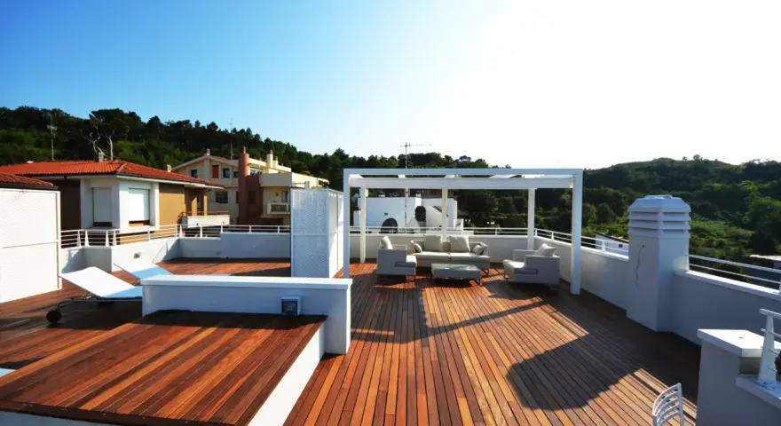 Terrazza sul tetto idee: un salotto all'aperto con divani, poltrone e tavolino sotto un pergolato bianco. Sdraio e vista su case e colline verdi.