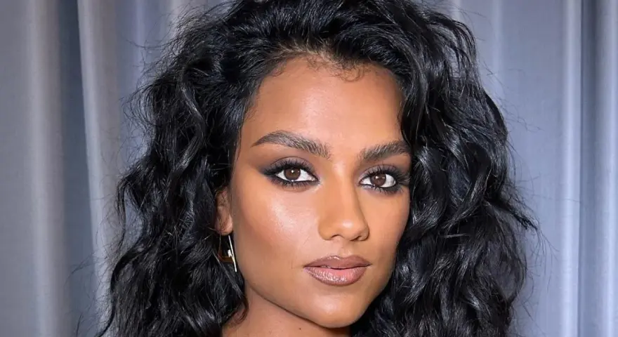 Capelli neri e ondulati, lucidi grazie al hair oiling, incorniciano il viso di una donna con trucco intenso.