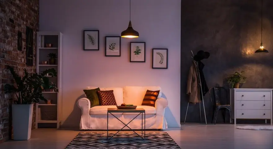 Un divano bianco accogliente, con cuscini colorati, in un soggiorno con mattoni a vista e quadri botanici. Atmosfera di puro stile cozy.