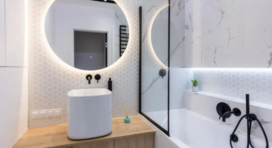 Moderno bagno con lavabo bianco su mobile in legno, specchio rotondo illuminato e vasca da bagno. Ottime bagno cieco idee.