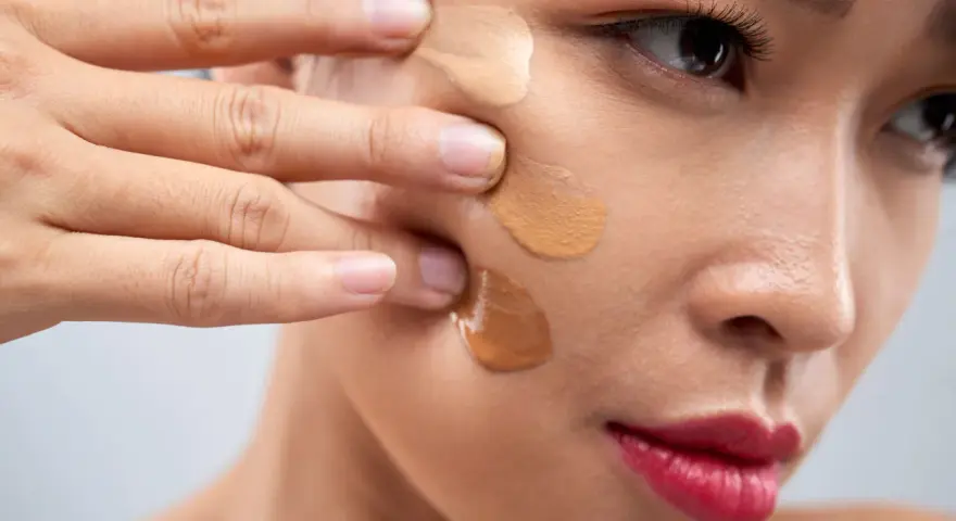 Dita che sfumano campioni di fondotinta sulla guancia per capire come scegliere il colore del fondotinta perfetto.