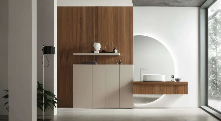 Bagno elegante e raffinato con mobile in legno, lavabo sospeso, specchio circolare retroilluminato e un tocco di verde da una pianta.