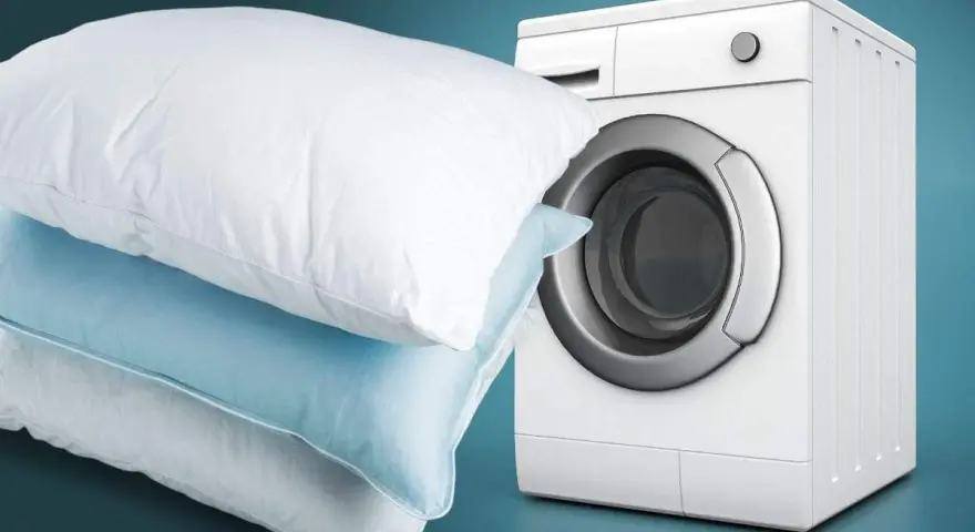 Impara come lavare i cuscini in lavatrice per un sonno fresco e igienico. Cuscini bianchi e azzurri accanto a una lavatrice bianca.