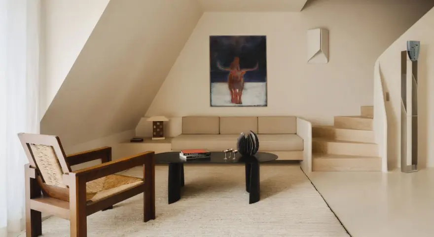 Arredamento minimal soggiorno: poltrona in legno e paglia, divano beige, tavolino nero con libri e scultura, quadro astratto con toro.