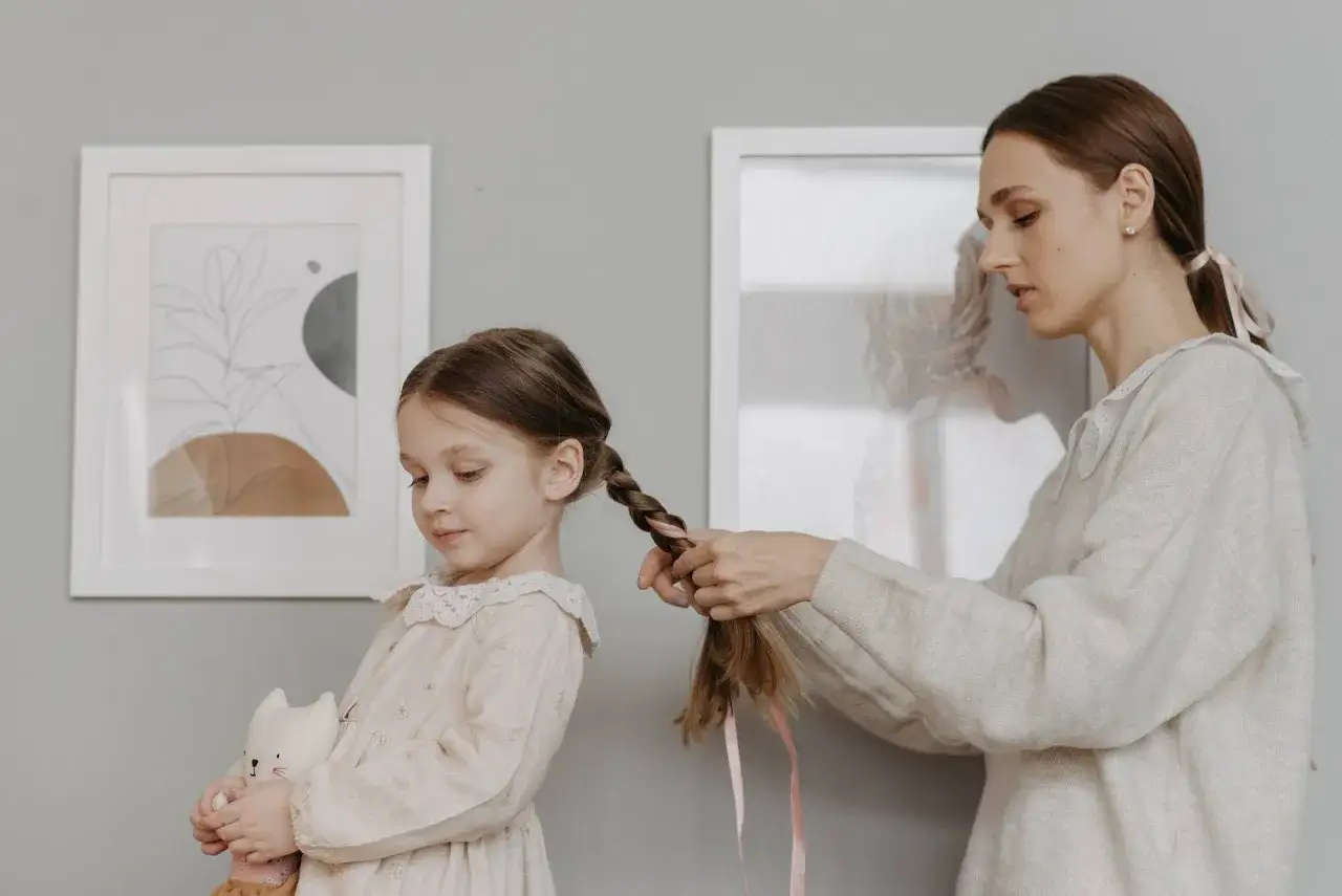 Mamma intreccia i capelli della bambina, creando bellissime acconciature. La piccola tiene un pupazzo a forma di gatto.