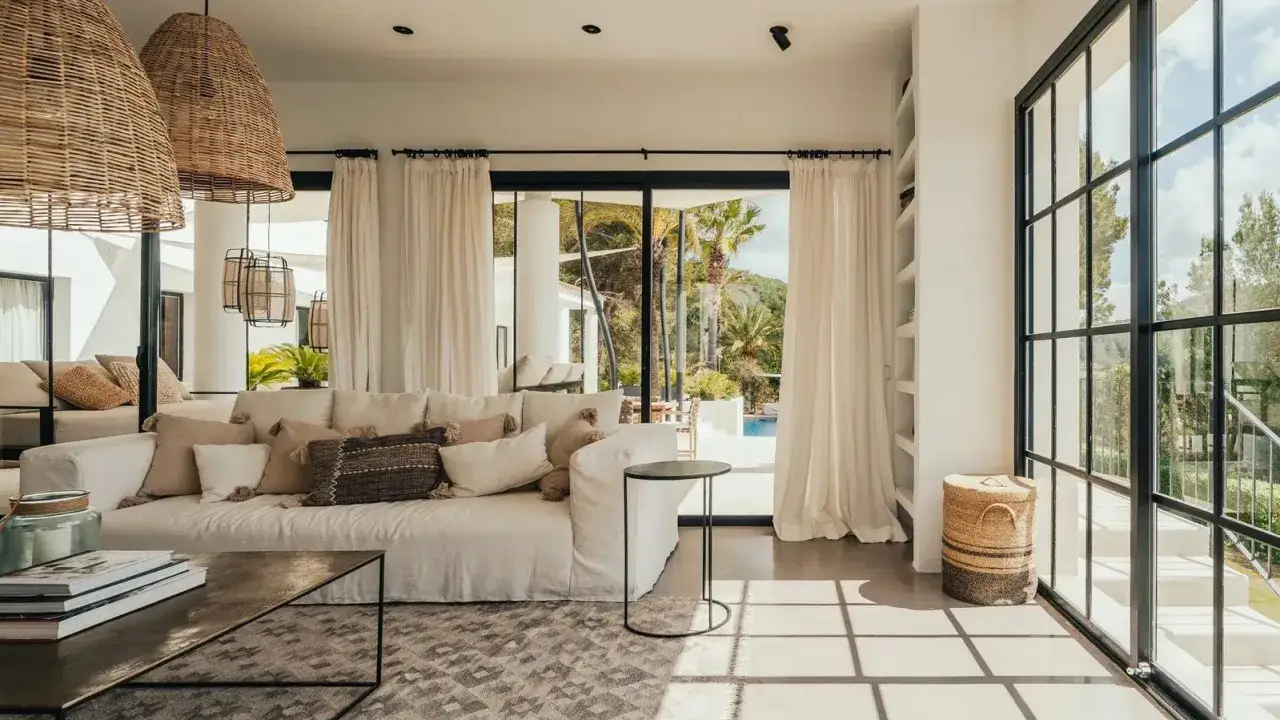 Luminoso soggiorno con divano bianco, cuscini in lino e rattan, tavolino in metallo. L'arredamento di queste case al mare evoca relax e stile mediterraneo.