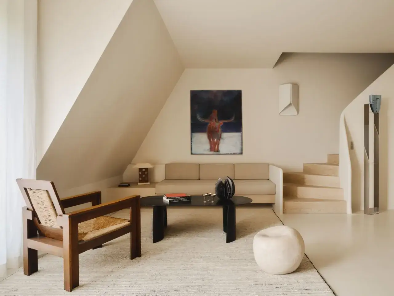 Arredamento minimal soggiorno con poltrona in legno, divano beige, tavolino nero e quadro astratto.