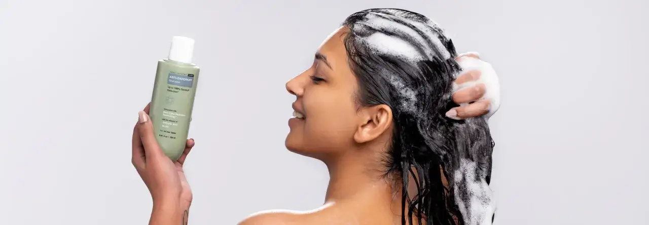 Donna sorride mentre si lava i capelli con shampoo antiforfora. Scopri come togliere la forfora in 5 minuti con questo prodotto.