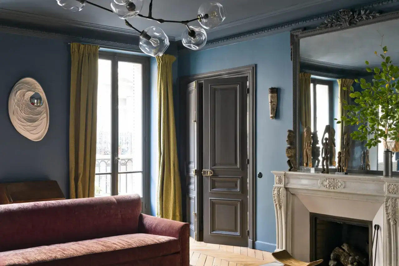 Soggiorno con divano bordeaux, pareti blu balena e tendaggi ocra. Un camino in marmo e sculture africane completano l'arredo.