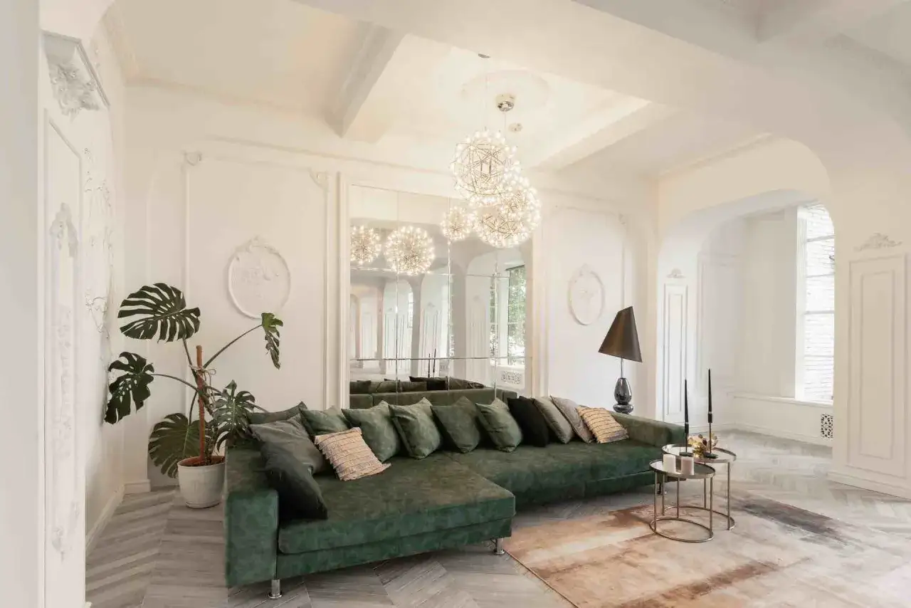 Eleganti case stile Liberty interni: divano verde smeraldo, piante rigogliose, specchi e lampadari sferici creano un'atmosfera sofisticata.