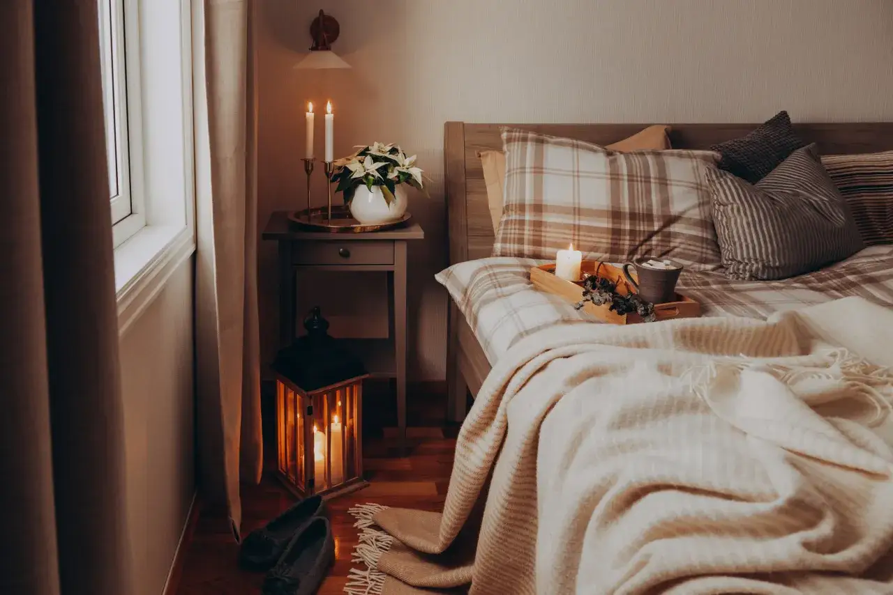 Accogliente camera da letto con candele accese, plaid morbido e pantofole, un vero invito a creare camere da letto da sogno.