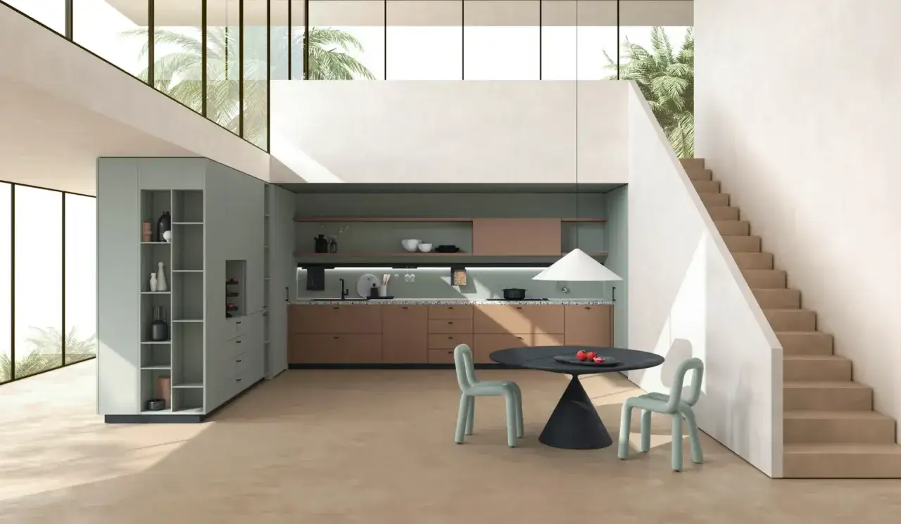 Cucine colorate con mobili verdi e color terra, un tavolo nero con sedie azzurre e una scala bianca in un ambiente luminoso con palme.