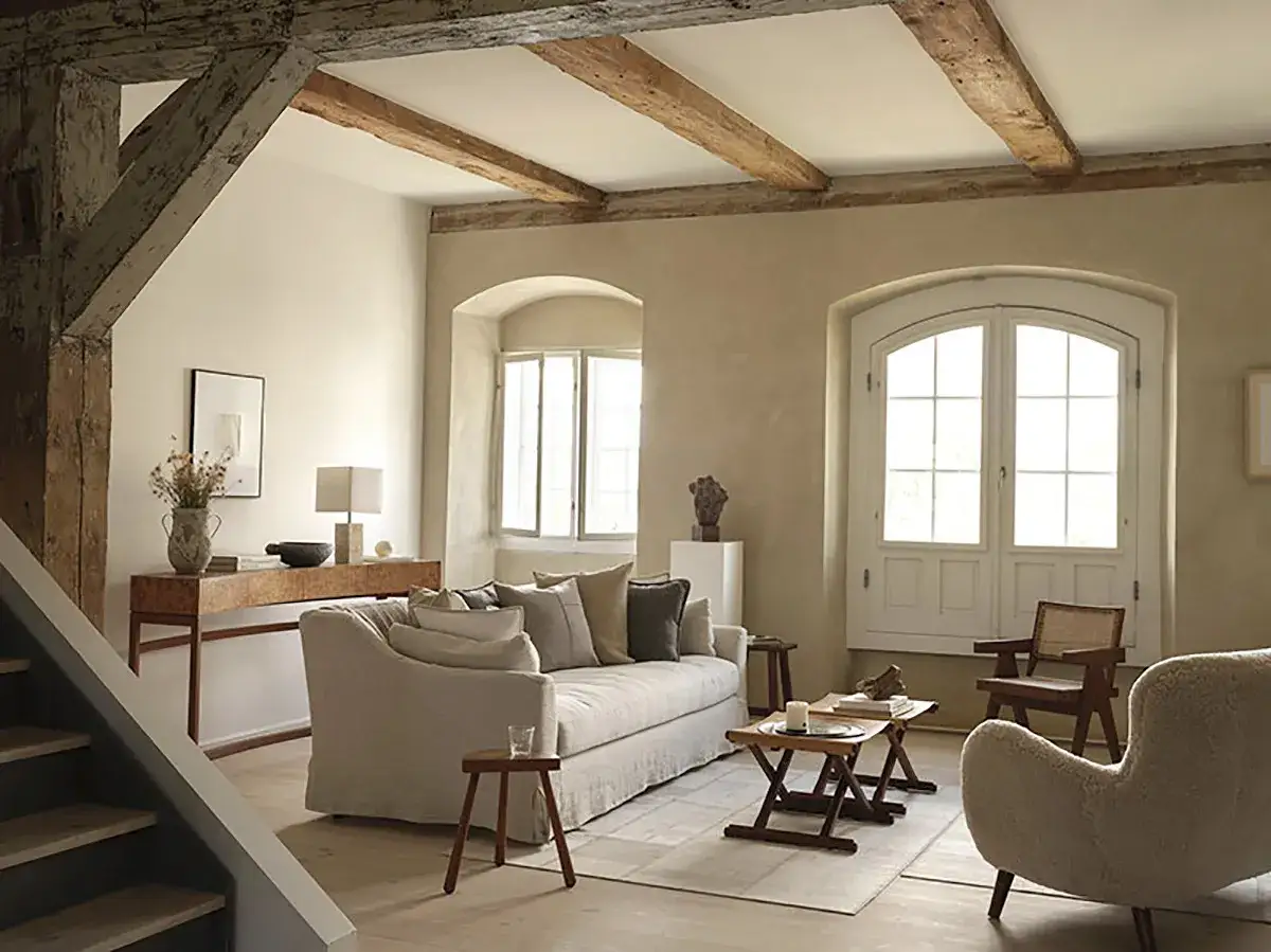 Soggiorno con divano bianco, tavolini in legno e poltrona in lana. L'arredamento casa stile moderno si fonde con travi a vista e archi in pietra.