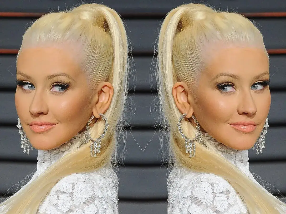 Christina Aguilera con capelli raccolti in una coda alta, di un brillante colore platino, indossa orecchini scintillanti e un abito bianco.