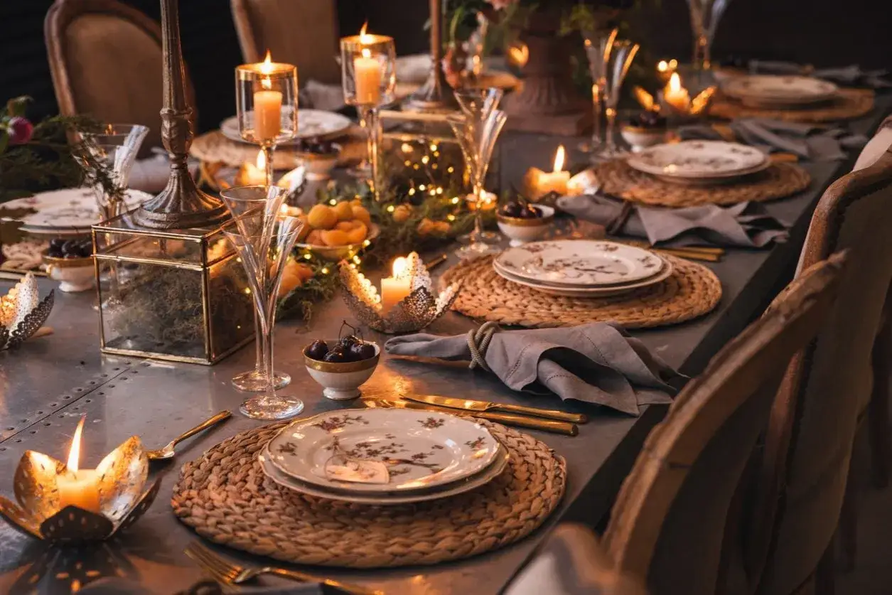 Tavola apparecchiata con candele accese, piatti decorati, frutta e luci soffuse. Un'atmosfera calda e accogliente per cene speciali.